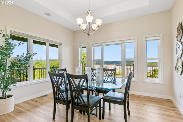 dining room featuring light wood-style floors, a raised ceiling, a chandelier, and baseboards