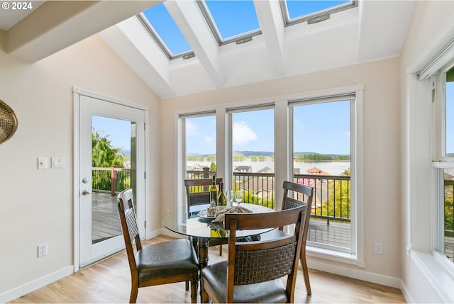 dining room with baseboards, vaulted ceiling with skylight, a water view, and light wood-style floors