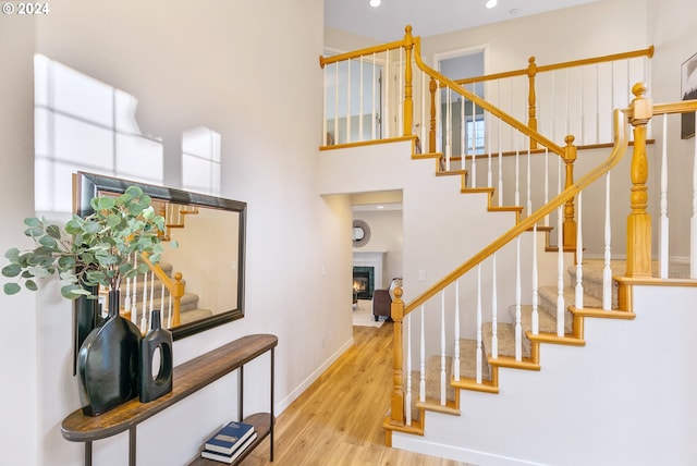 stairway with a glass covered fireplace, a towering ceiling, baseboards, and wood finished floors