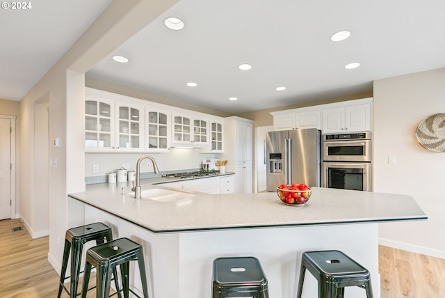 kitchen with a sink, appliances with stainless steel finishes, light wood-type flooring, a kitchen bar, and glass insert cabinets