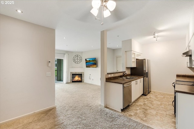 kitchen featuring under cabinet range hood, dark countertops, a ceiling fan, a glass covered fireplace, and appliances with stainless steel finishes