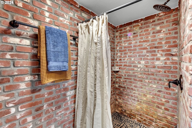 bathroom with a shower with shower curtain and brick wall