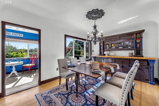 dining area featuring light wood-type flooring, a chandelier, a textured ceiling, and indoor bar