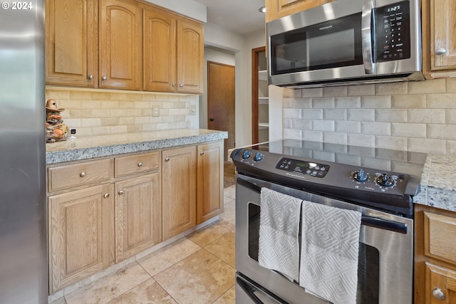 kitchen featuring light stone countertops, light tile patterned floors, appliances with stainless steel finishes, and tasteful backsplash