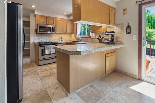 kitchen featuring kitchen peninsula, appliances with stainless steel finishes, a healthy amount of sunlight, and backsplash