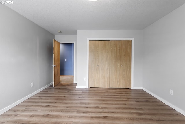 unfurnished bedroom with a textured ceiling, light hardwood / wood-style flooring, and a closet