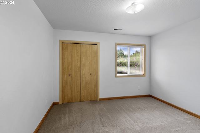 unfurnished bedroom featuring a textured ceiling, light carpet, and a closet