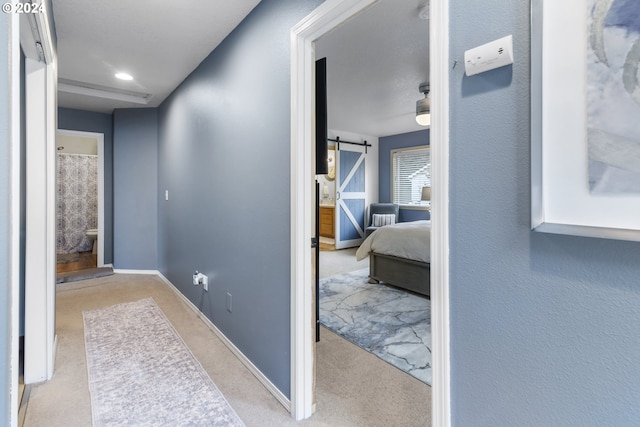 corridor featuring a barn door and light colored carpet