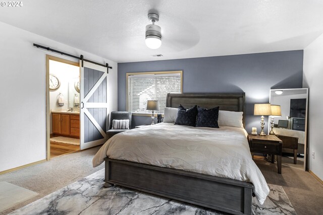 bedroom featuring ceiling fan, a barn door, carpet floors, and connected bathroom