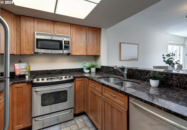 kitchen with appliances with stainless steel finishes, dark stone counters, and sink