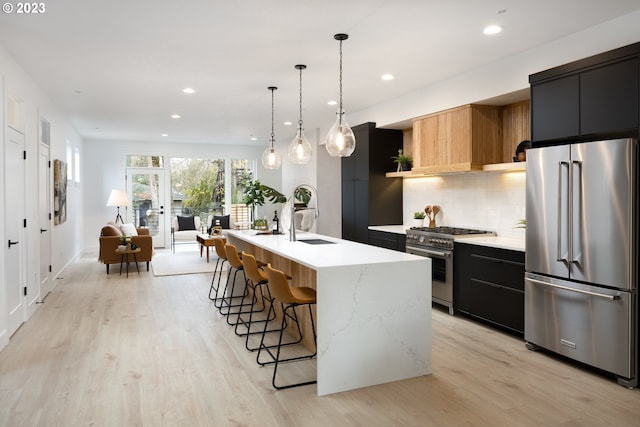 kitchen featuring a kitchen island with sink, pendant lighting, light hardwood / wood-style flooring, premium appliances, and tasteful backsplash