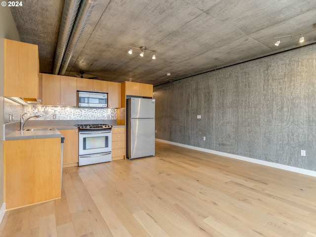 kitchen featuring sink, backsplash, track lighting, appliances with stainless steel finishes, and light wood-type flooring