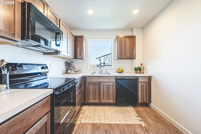 kitchen featuring black appliances, a textured ceiling, sink, and light hardwood / wood-style flooring