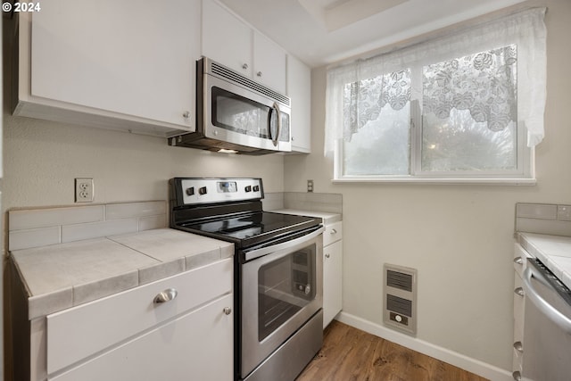 kitchen with light wood-type flooring, stainless steel appliances, heating unit, tile countertops, and white cabinetry