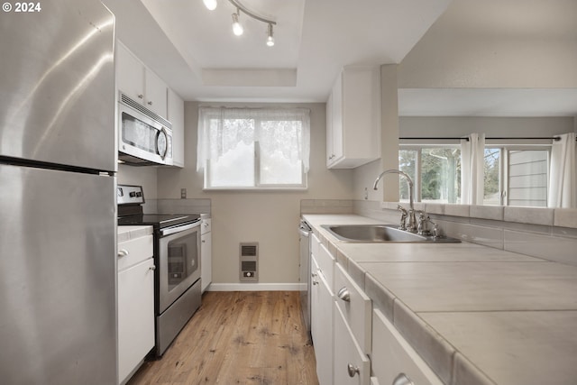 kitchen featuring appliances with stainless steel finishes, a tray ceiling, sink, light hardwood / wood-style flooring, and white cabinets