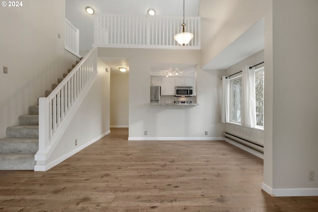 unfurnished living room with light wood-type flooring, a high ceiling, and a baseboard heating unit