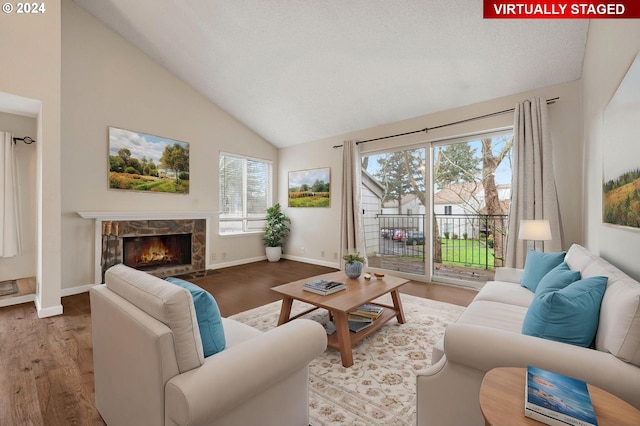 living room with light hardwood / wood-style floors, a stone fireplace, and lofted ceiling