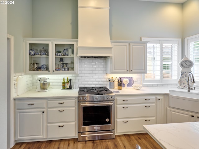 kitchen featuring stainless steel gas range, sink, white cabinetry, custom range hood, and backsplash