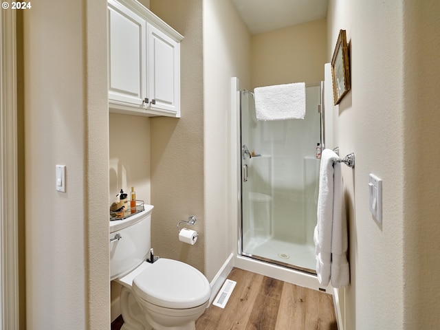 bathroom with hardwood / wood-style floors, a shower with door, and toilet