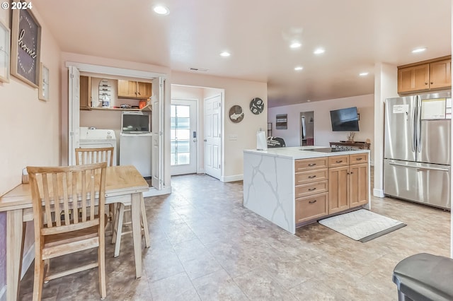 kitchen with light stone countertops, independent washer and dryer, and stainless steel refrigerator