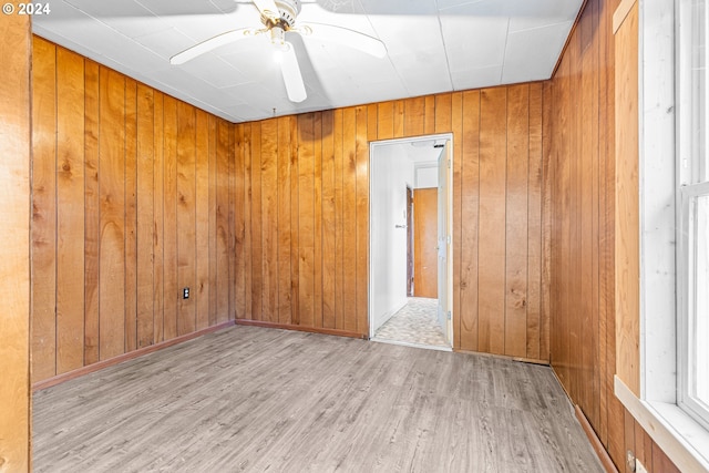 unfurnished room with light hardwood / wood-style flooring, ceiling fan, and wooden walls