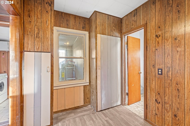 corridor with washer / dryer, light hardwood / wood-style floors, and wooden walls