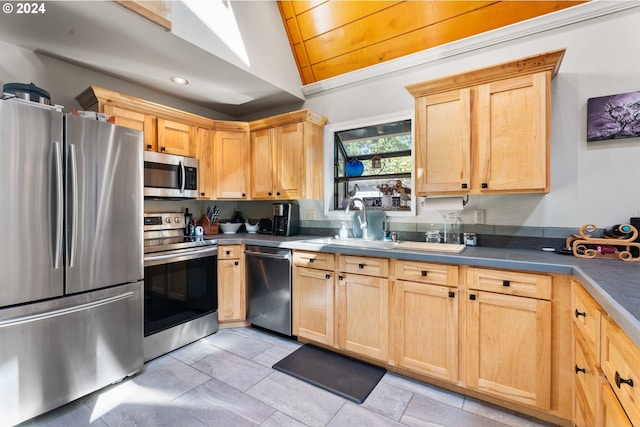 kitchen featuring stainless steel appliances, dark countertops, lofted ceiling, light brown cabinetry, and a sink