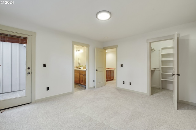 unfurnished bedroom featuring a spacious closet, a closet, light colored carpet, and ensuite bathroom