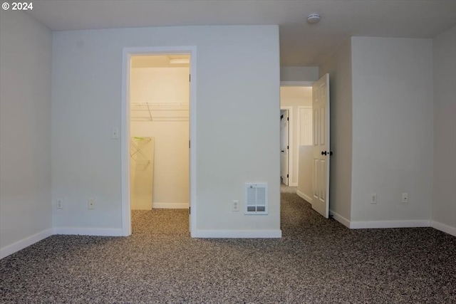 unfurnished bedroom featuring a spacious closet, dark carpet, and a closet