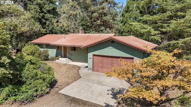 single story home featuring a tiled roof, a chimney, an attached garage, and driveway