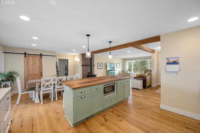 kitchen featuring a barn door, light hardwood / wood-style flooring, butcher block countertops, stainless steel microwave, and green cabinets