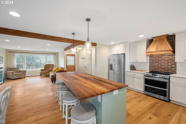 kitchen featuring premium range hood, stainless steel appliances, light hardwood / wood-style floors, hanging light fixtures, and a breakfast bar area