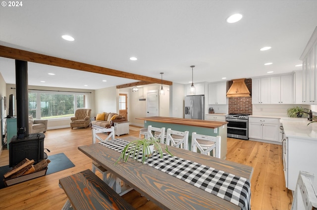 dining space with beam ceiling, light wood-type flooring, a wood stove, and sink