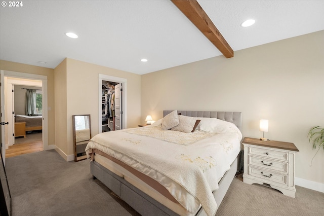 bedroom featuring beam ceiling, a spacious closet, a closet, and light colored carpet