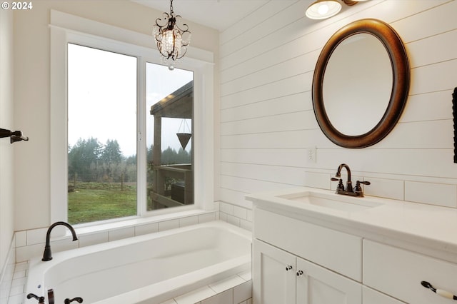 bathroom featuring vanity, tiled tub, and a chandelier