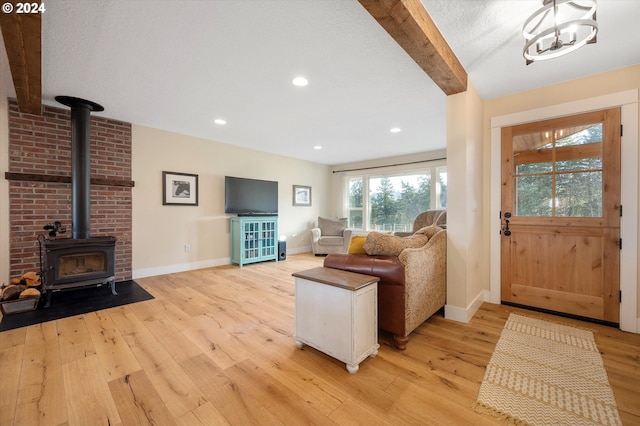 living room with beam ceiling, a wood stove, a chandelier, light hardwood / wood-style floors, and a textured ceiling