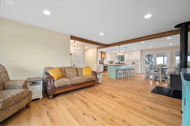 living room featuring beam ceiling, a wood stove, and light wood-type flooring