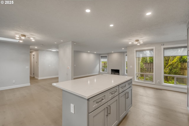 kitchen featuring gray cabinets, a center island, a large fireplace, a textured ceiling, and light wood-type flooring