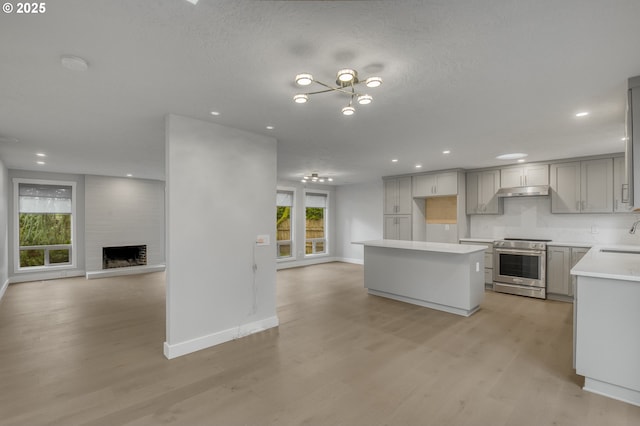 kitchen with stainless steel range, gray cabinets, a kitchen island, a fireplace, and light hardwood / wood-style floors