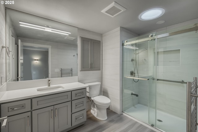 bathroom with hardwood / wood-style floors, a shower with shower door, tile walls, vanity, and toilet