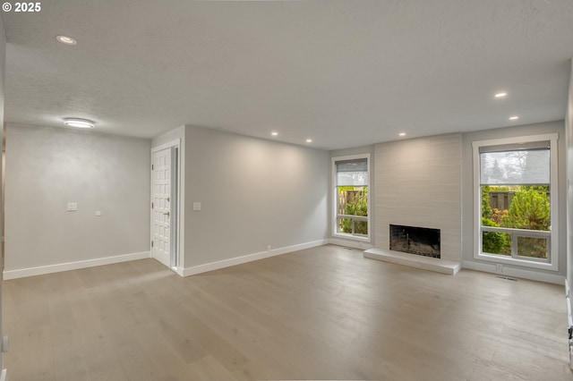 unfurnished living room featuring a high end fireplace, light hardwood / wood-style flooring, and a textured ceiling