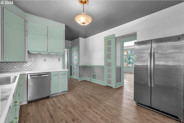 kitchen featuring decorative backsplash, stainless steel appliances, decorative light fixtures, and light hardwood / wood-style flooring