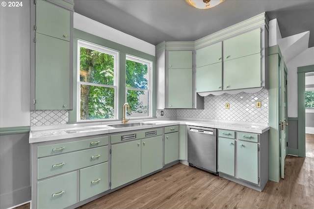 kitchen with light wood-type flooring, backsplash, stainless steel dishwasher, sink, and green cabinetry