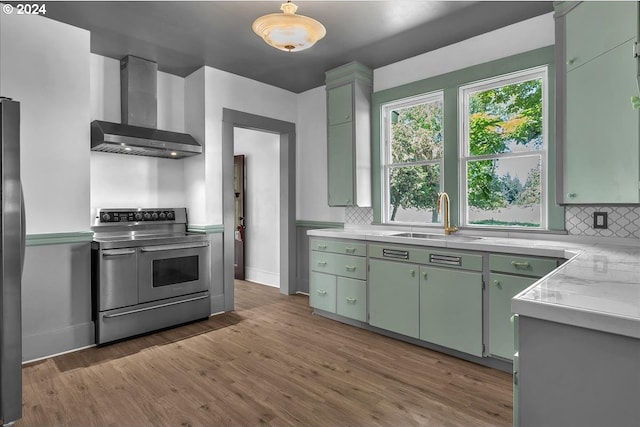 kitchen featuring stainless steel range with electric stovetop, wall chimney range hood, sink, decorative backsplash, and wood-type flooring