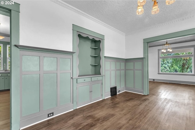 unfurnished living room with crown molding, dark wood-type flooring, a textured ceiling, and an inviting chandelier