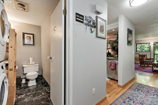 bathroom featuring wood-type flooring, toilet, stacked washer / drying machine, and a textured ceiling