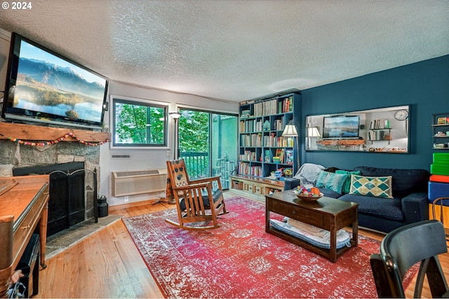 living room with a textured ceiling, a stone fireplace, hardwood / wood-style floors, and a wall unit AC