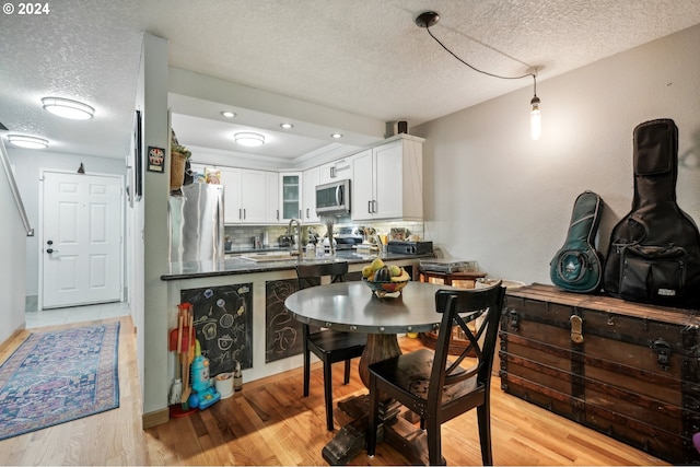 kitchen featuring a textured ceiling, white cabinetry, appliances with stainless steel finishes, light wood-type flooring, and decorative backsplash