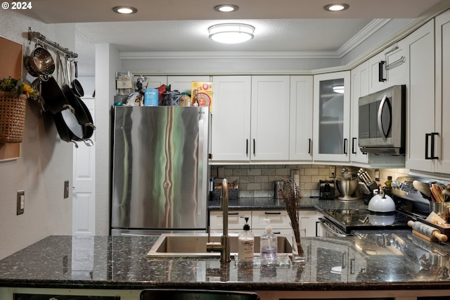 kitchen with ornamental molding, tasteful backsplash, white cabinetry, stainless steel appliances, and dark stone counters