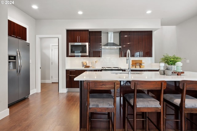 kitchen featuring dark hardwood / wood-style floors, stainless steel appliances, sink, wall chimney range hood, and a kitchen bar